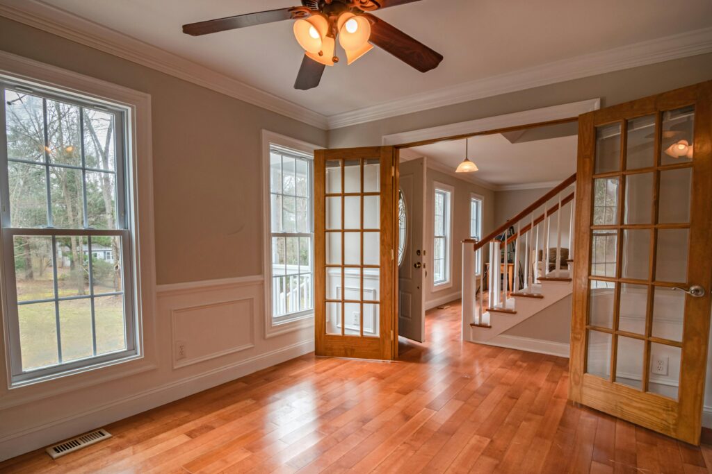 Spacious living room with wooden French doors and ceiling fan, showcasing contemporary interior design.